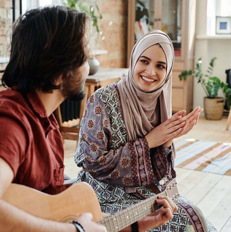 A couple enjoys music at home with an acoustic guitar, fostering a warm and romantic atmosphere.