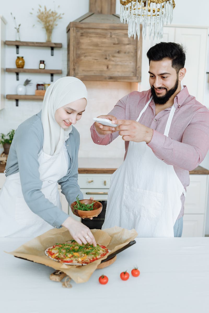 Happy couple cooking together, capturing a pizza creation in a modern kitchen setting.