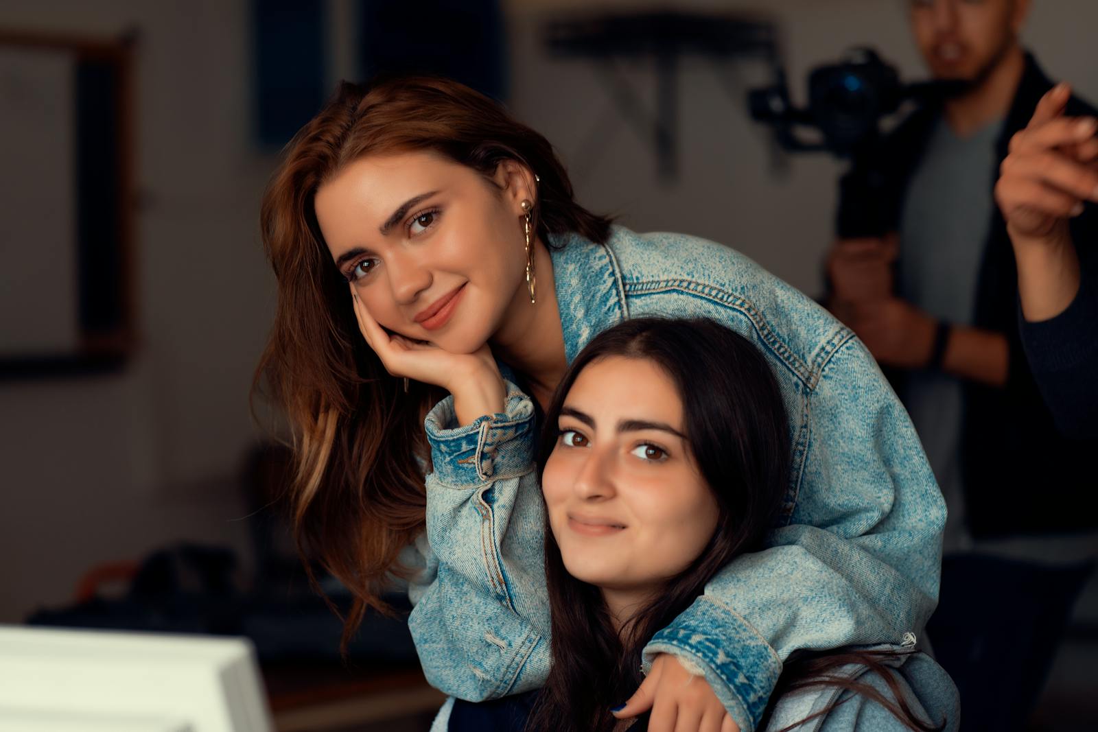 Two women in denim jackets smiling warmly, embracing indoors. Captures friendship and joy.